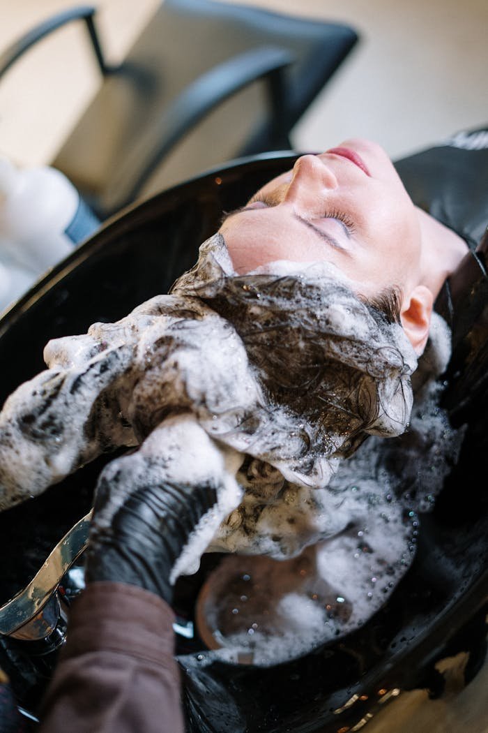 A woman getting her hair washed at a salon sink by a professional stylist wearing black gloves.